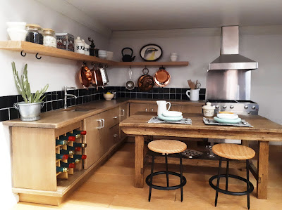 1/12 scale modern miniature kitchen with cupboards in wood, a central workbench and black tiles.