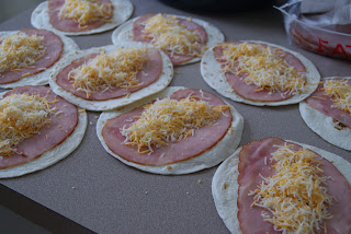 Nine four tortillas played flat and topped with a slice of ham, and shredded cheese.