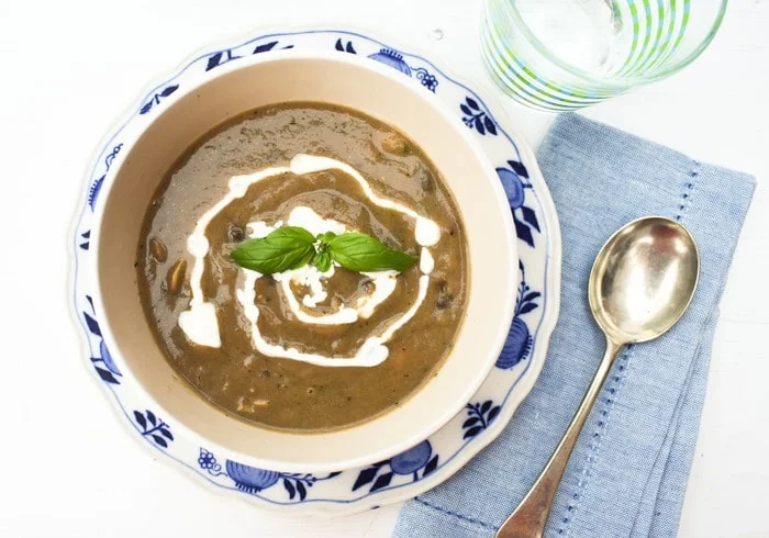 A bowl of mushroom soup topped with a swirl of cream and a sprig of fresh basil