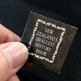 Hand holding a one-twelfth scale book titled 'New Zealand's smallest history'