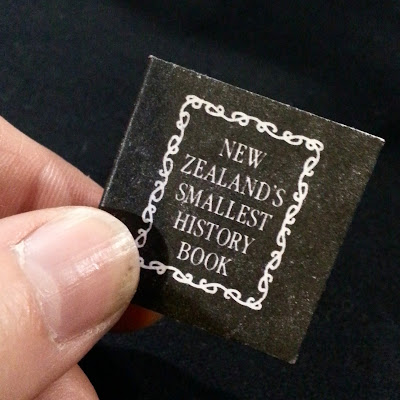 Hand holding a one-twelfth scale book titled 'New Zealand's smallest history'