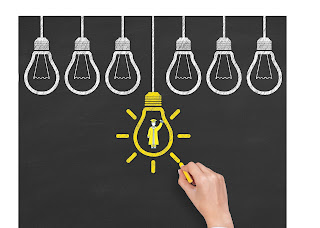 chalk board with a line of white light bulb drawings and one yellow light bulb with a college graduate holding up a diploma lighting up the yellow lightbulb