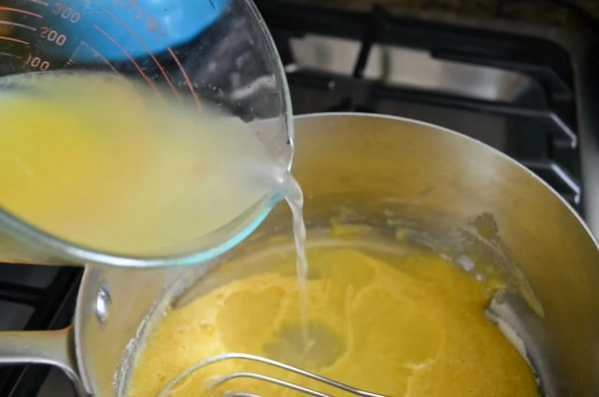 Pineapple Juice being whisked into flour egg mixture in a saucepan.