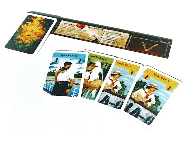 na zdjęciu planszetka gracza, na niej leżą zakryte karty a cztery karty leża odkryte na stole