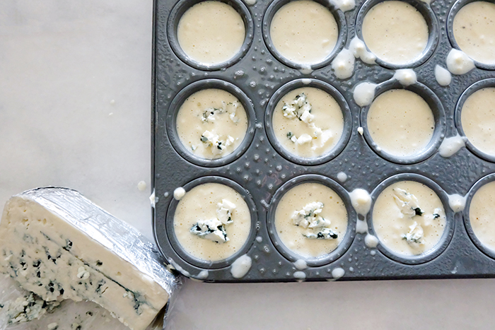 dropping bits of bleu cheese into batter in muffin tin