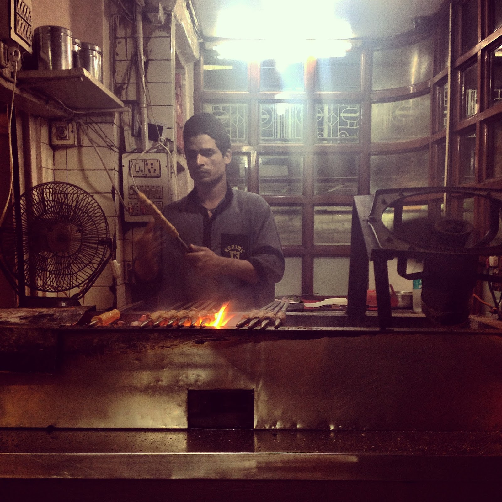 man holding kebab over fire at karims in old delhi