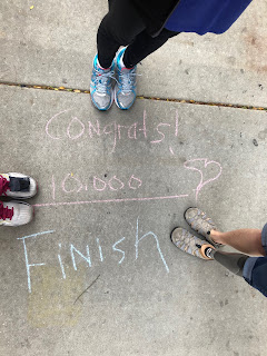 3 sets of feet, one with a prosthetic leg, gathered around a patch of sidewalk where it's written "Congrats 10,000!  Finish."