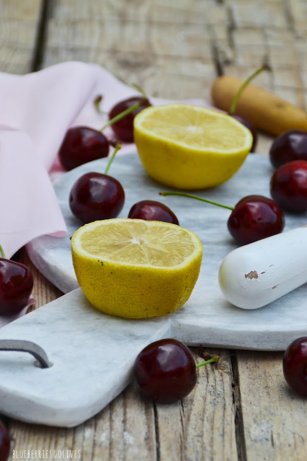 INGREDIENTES PARA LIMONADA DE CEREZAS, RODAJAS DE LIMÓN Y CEREZAS, TABLA CORTAR MÁRMOL, PAÑO ROSA
