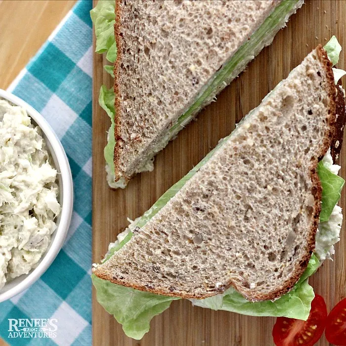 southern style chicken salad recipe in white bowl to the left and a sandwich cut diagonally on a board with Southern style chicken salad and lettuce on whole grain bread to the right