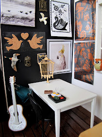 Modern dolls house miniature cafe scene, with black and white walls, wooden floor, white and beech tables, black chairs and a gallery wall of bird-related art.