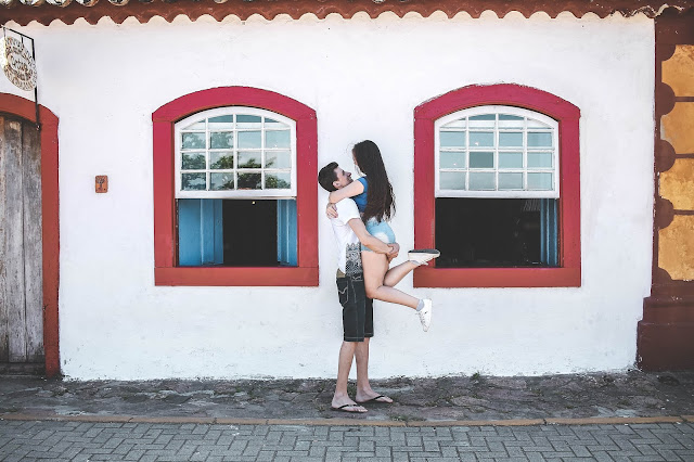 Casal abraçado em frente a casa branca com vermelho