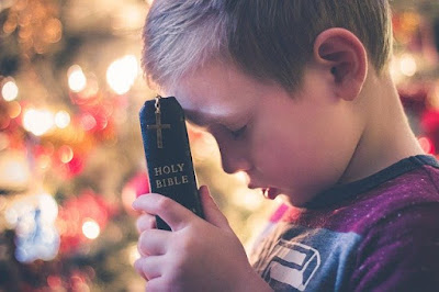 menino orando com a Bíblia nas mãos