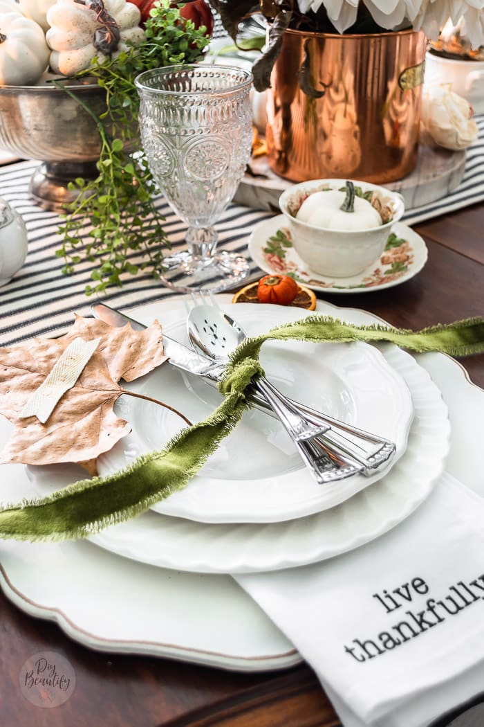 table decorated for Thanksgiving with white plates, green ribbon, pumpkins and stamped leaf place cards