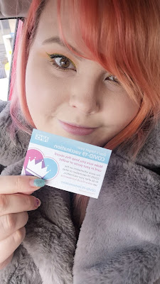 Selfie of Nici holding up her vaccination card with pink hair and green eyeliner