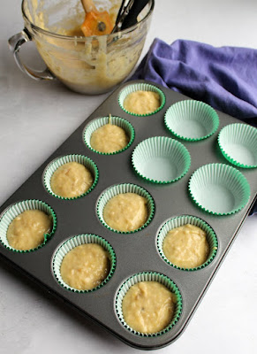 scooping banana cupcake batter into cupcake tray with paper liners