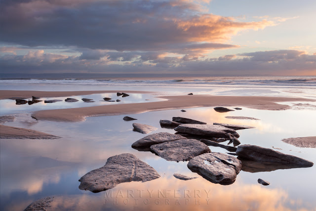 Clouds reflect around beach rocks at Dunraven Bay in South Wales at Sunset by Martyn Ferry Photography