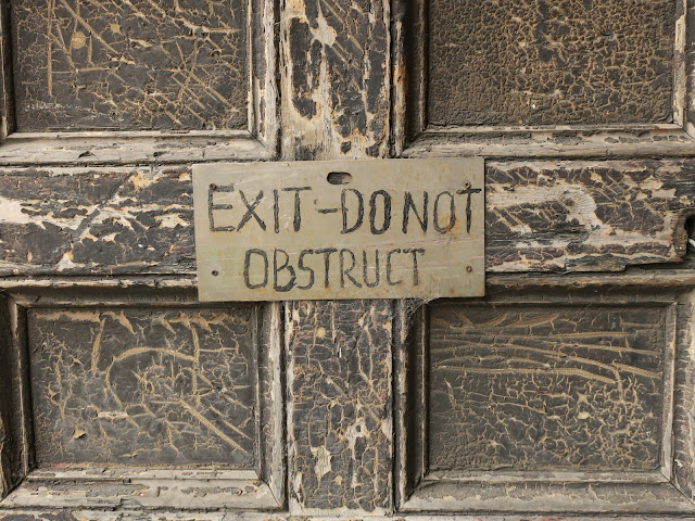 Wooden door with flaking brown paint and notice - EXIT - DO NOT OBSTRUCT