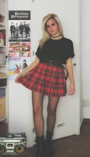 Estilo grunge con camiseta negra, falda de tablas tartán, medias de red grande, botas estilo militar y cazadora vaquera