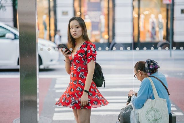 バス停で携帯電話を持って立っている赤いミニドレスの女性。