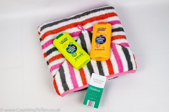 A folded up children's towel with hood and stripes in grey, orange and pink and 2 bottles of children's shampoo