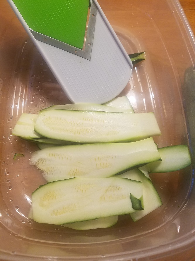 this is a mandolin used to sliced vegetables and the zucchini is in a plastic dish