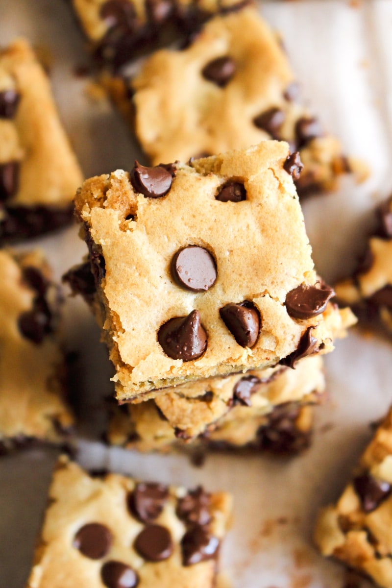 Brown Butter Chocolate Chip Cookie Bars | The Two Bite Club | #chocolate #cookiebars Top view of brown butter cookie bars squares stacked on a piece of parchment paper.
