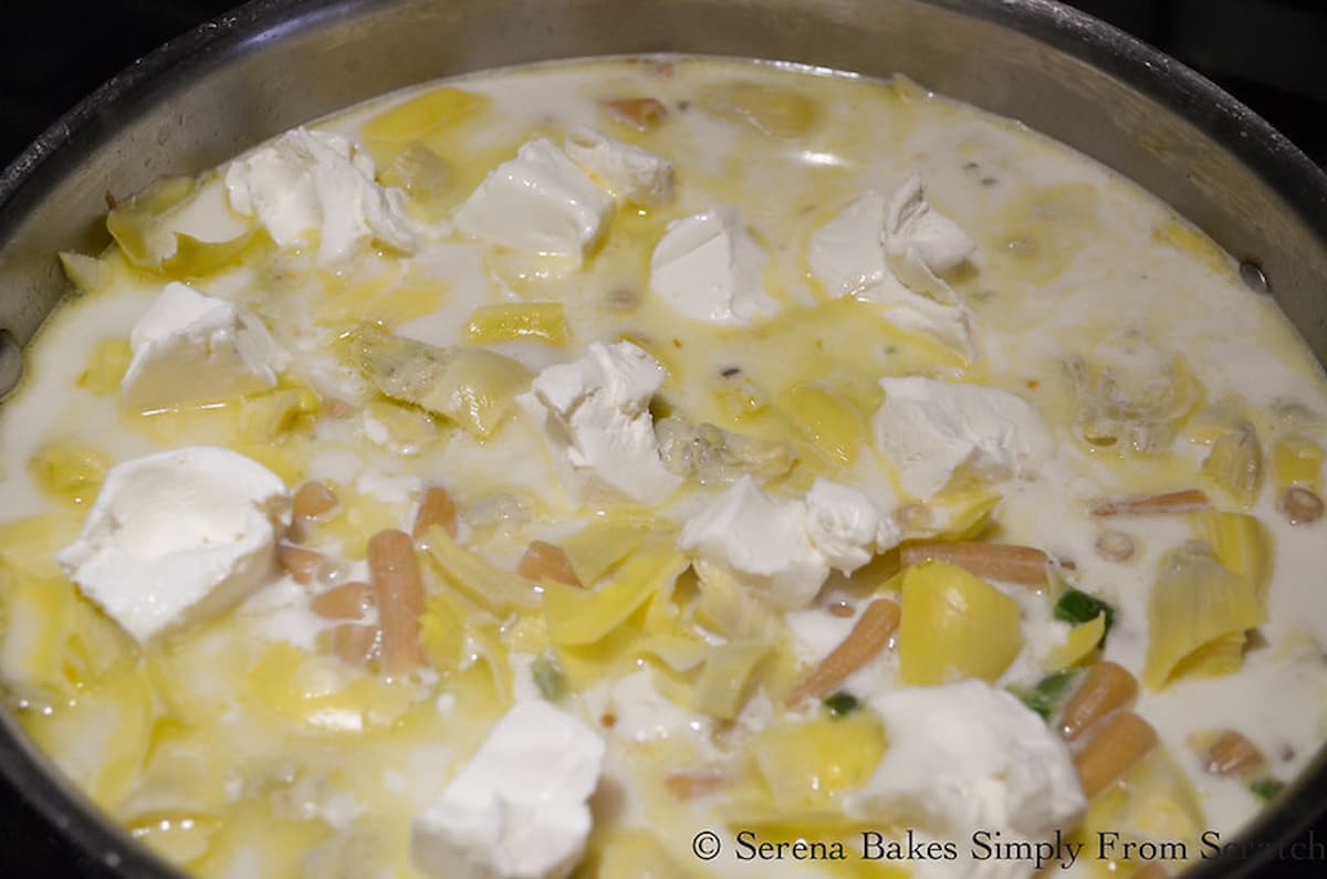 A skillet with pasta, chicken broth, Half and Half, Milk, Cream Cheese, Artichoke Hearts, and Red Pepper Flakes,