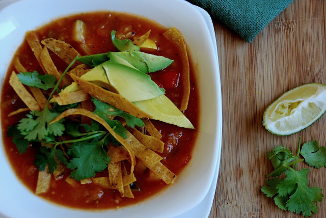 red soup topped with sliced avocado, tortilla strips, and cilantro in a white bowl viewed from overhead