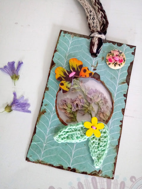 Etiqueta colgante con flor prensada de la alfalfa, unas hojitas de ganchillo y unos botones en forma de flor