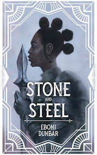 A Black woman in armor stands in profile clutching a spear vertically with her lips almost touching the tip of the spearhead.