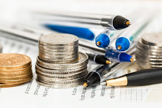 A stock image of stacked coins and piled ink pens, resting on what appears to be instructions for an official form.