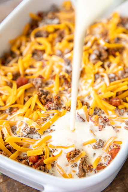 Low Carb Taco Casserole - low on carbs but high on taste! SO good! Everyone cleaned their plate and asked for seconds!! Ground beef, taco seasoning, diced tomatoes and green chiles, cheddar cheese, eggs, sour cream, and heavy cream. It is like a quiche without the crust. Ready in 30 minutes. Can make ahead and refrigerate or freeze for later. #casserole #freezermeal #taco #mexican #lowcarb #keto #glutenfree pouring egg mixture into casserole dish