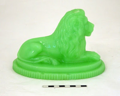 Seated green glass lion paper weight photographed under normal lighting conditions.