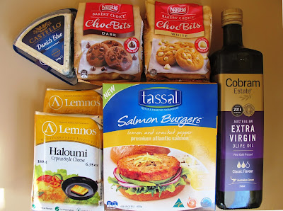 Luxury grocieries arranged on a kitchen bench, including blue cheese, chocolate baking bits, haloumi cheese, salmon burgers and olive oil.