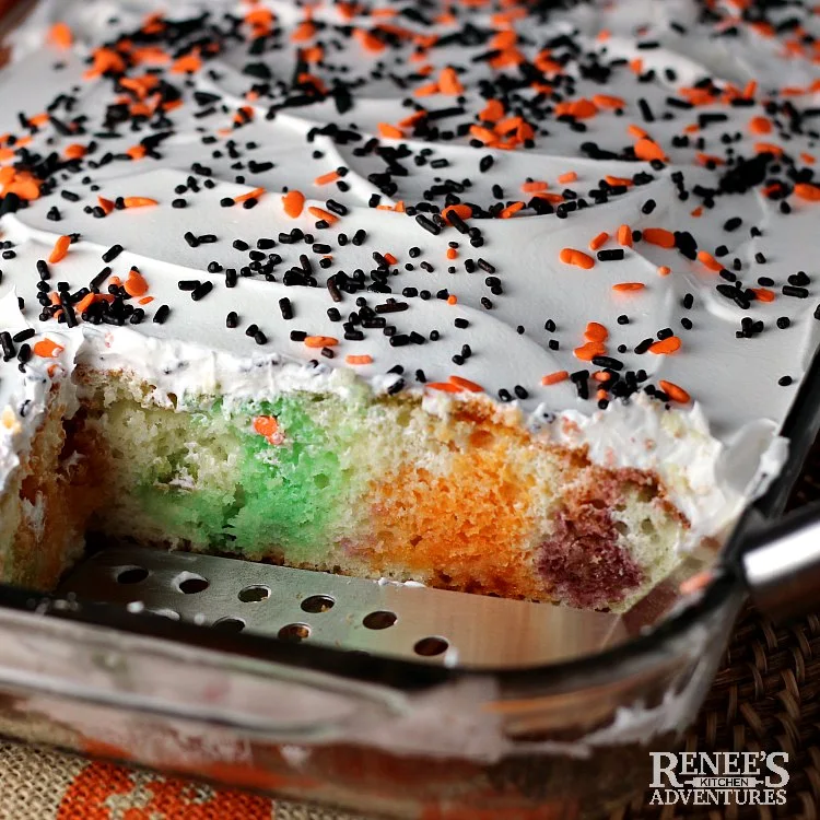 Pan of Halloween Jello Poke Cake by Renee's Kitchen Adventures with a few pieces cut out to show the colors of the gelatin in the cake