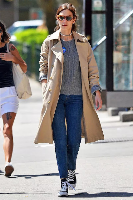The woman wears a trench coat and sweater.