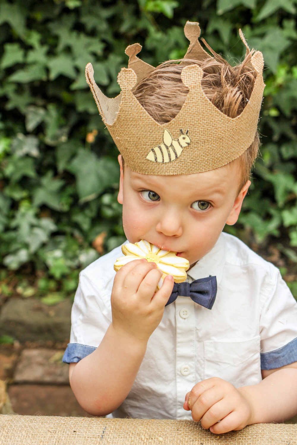 Birthday boy wearing bumblebee party crown hat and bow tie eating a daisy flower cookie For more boys and unisex kids first birthday party inspiration visit the Goldfields Girl blog