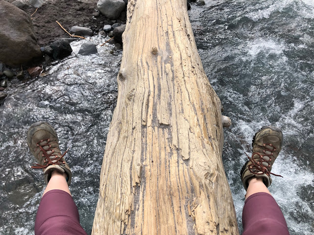 woman's legs dangling from log over flowing river