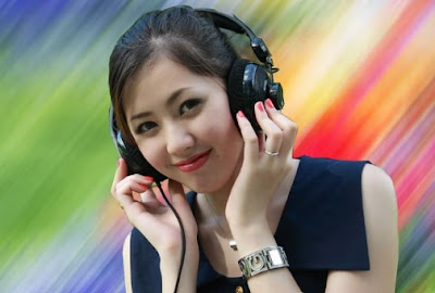 A picture of a person wearing headphones.  They have dark hair and are smiling.  The background is rainbow-coloured.