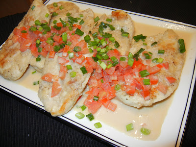 chicken breast on a white plate with tomatoes and green onions over the top with a cream sauce 