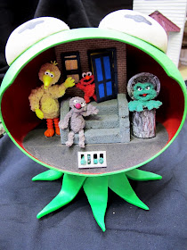 Plastic Kermit the Frog head with a scene from Sesame Street inside it.