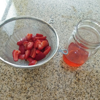 strawberries in a strainer next to strawberry infused simple syrup in a jar