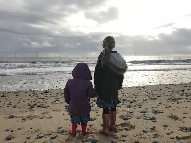 Sisters on holiday looking out to sea on a cold beach