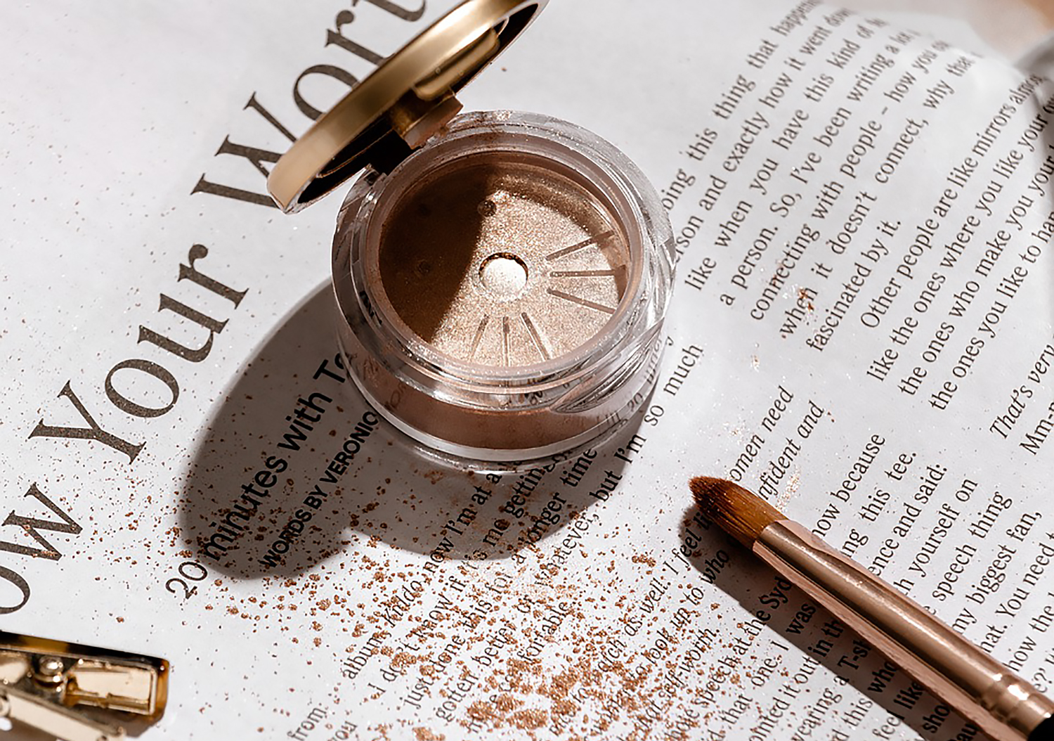 close-up of a glitter eyeshadow laying on top of a magazine, close to the makeup brush