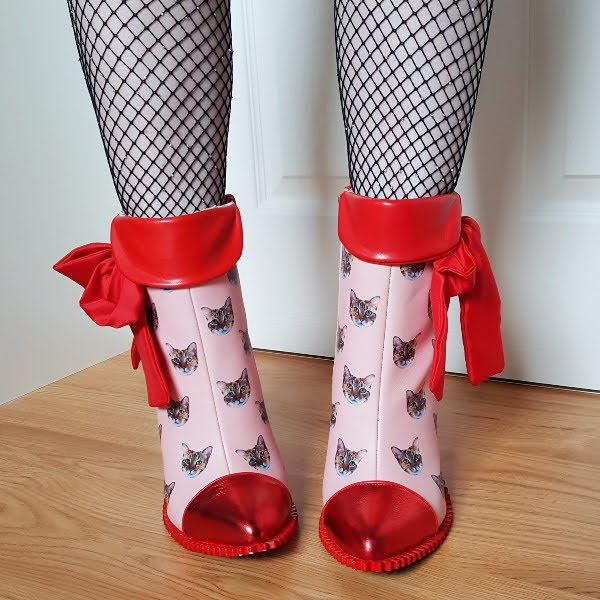 legs facing forward wearing fishnet tights and pink cat print ankle boots with contrast red metallic toe