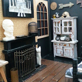 One-twelfth scale miniature scene, with a fireplace, distressed dresser and a bed in it.