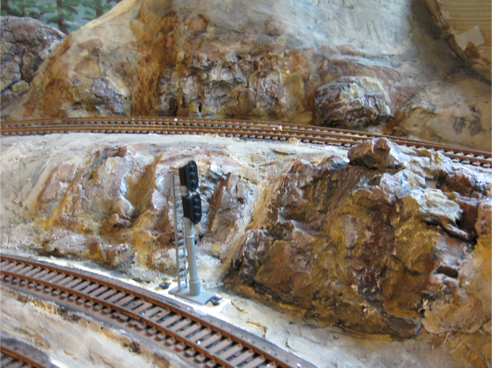 A wash of thinned black acrylic paint being applied to plaster hard shell terrain and plaster rock outcroppings