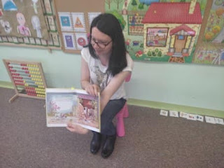 Zajęcia w przedszkolu. Pani bibliotekarka pokazuje przedszkolakom książkę o zwierzętach. Tło: talica korkowe z kolorowymi obrazkami.