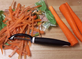 Fresh peeled carrots, and a vegetable peeler.