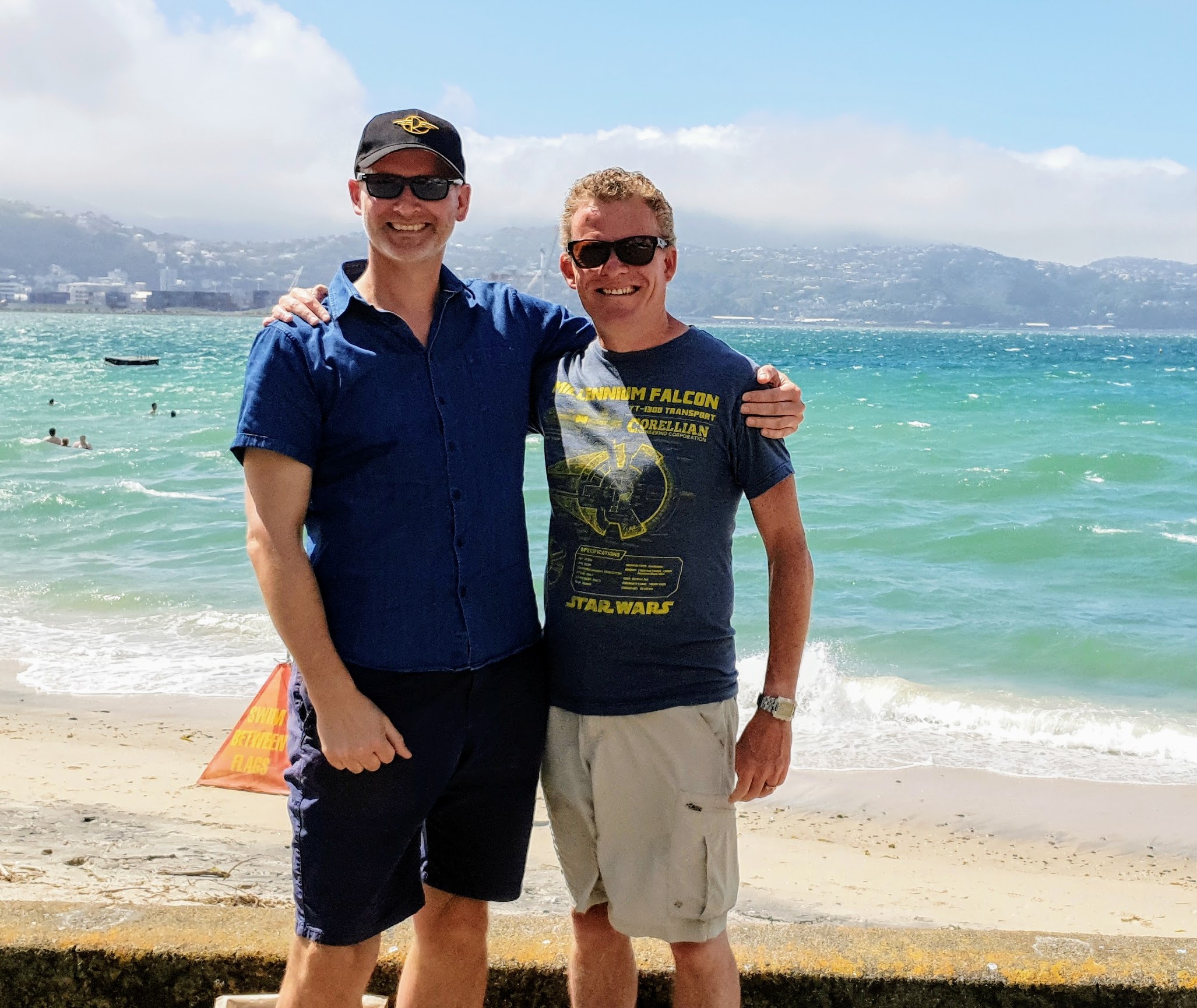 Friends hug on Oriental Parade with the Wellington Harbour behind